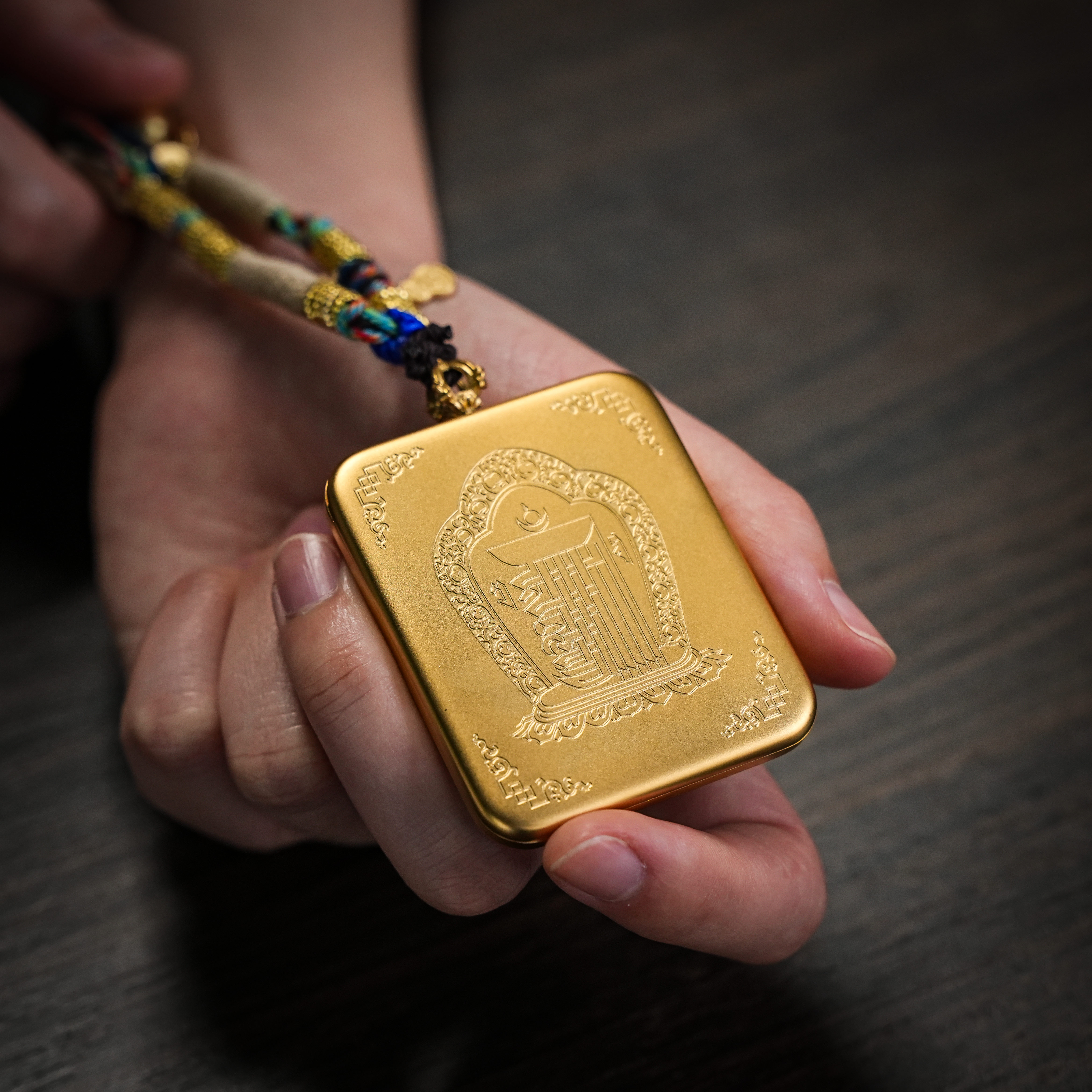 Brass thangka gau pendant resting in hand over scripture paper